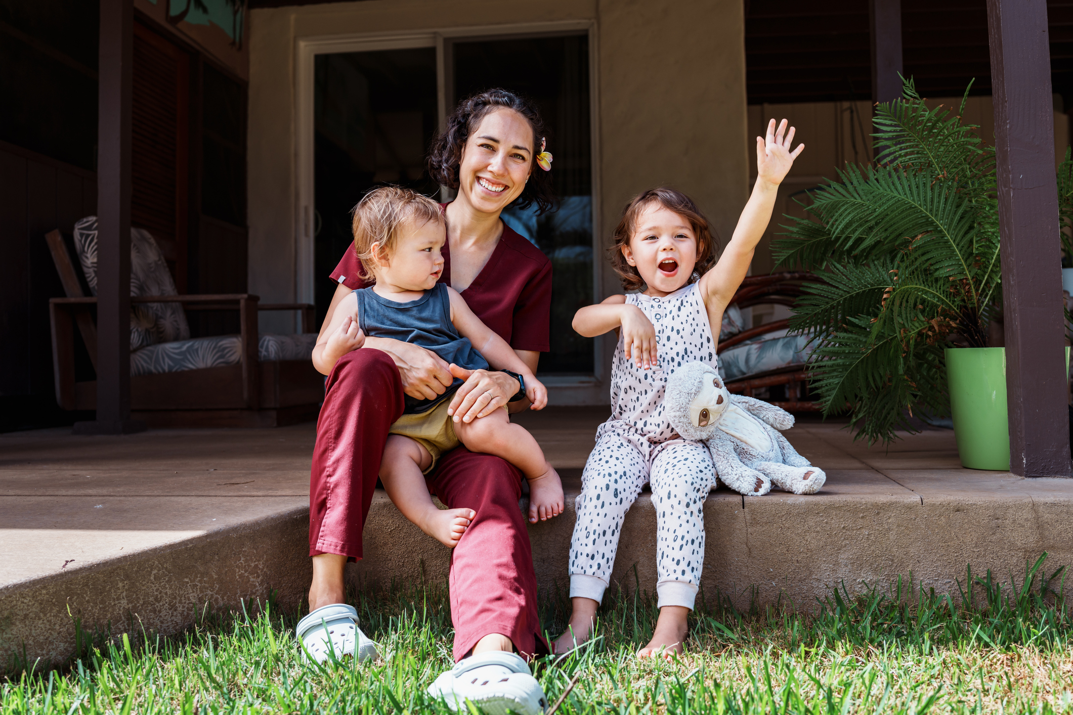 A female nurse of Hawaiian and Chinese descent sits outside on the back patio of her home and playfully interacts with her cheerful and cute Eurasian son and daughter after returning home from work.